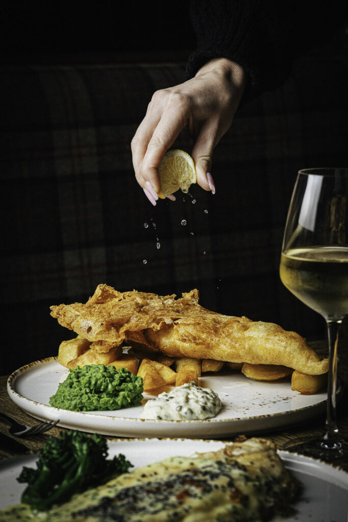 Fish and chips with mushy peas, tartar sauce, and a hand squeezing lemon
