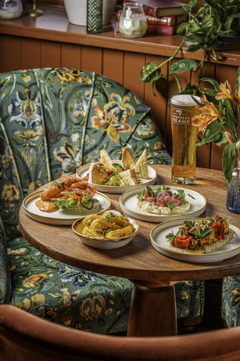 Small plates of tapas-style pub food with a pint of beer in a colourful pub interior