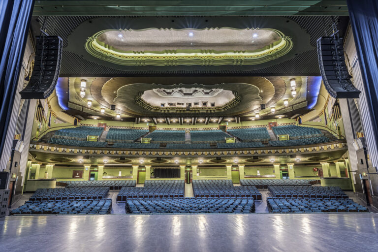 View from the stage inside the Eventim Apollo in Hammersmith, London — showing tiered turquoise seating and an ornate Art Deco ceiling.