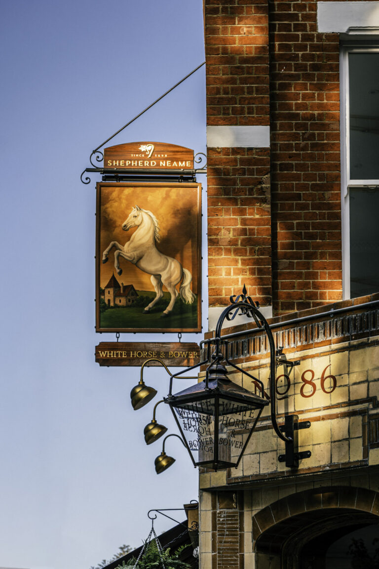 White Horse & Bower Shepherd Neame pub sign in London, featuring a rearing white horse painting on a traditional brick building.
