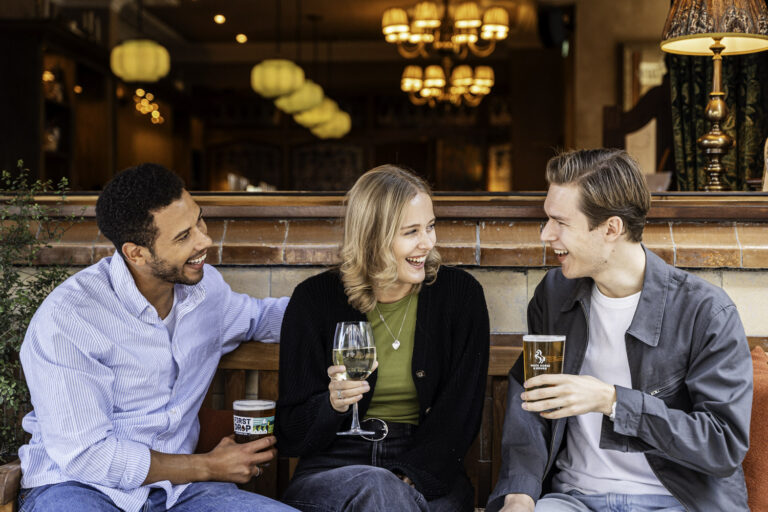 Three friends laughing and enjoying drinks together at The White Horse & Bower pub in London.