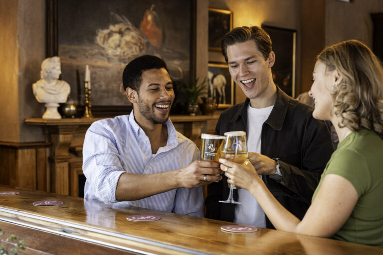 Three friends raising glasses and toasting with drinks at the bar inside The White Horse & Bower pub in London.