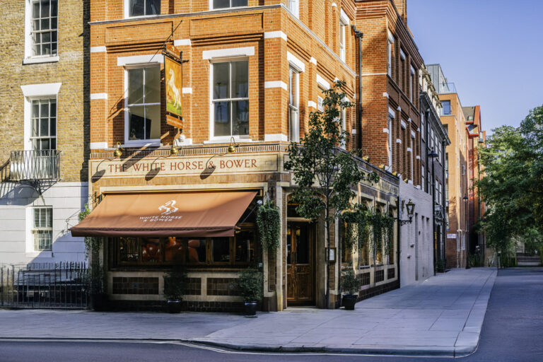 Street view of The White Horse & Bower pub in London, a red-brick building with large windows, hanging greenery, and a red canopy sign.