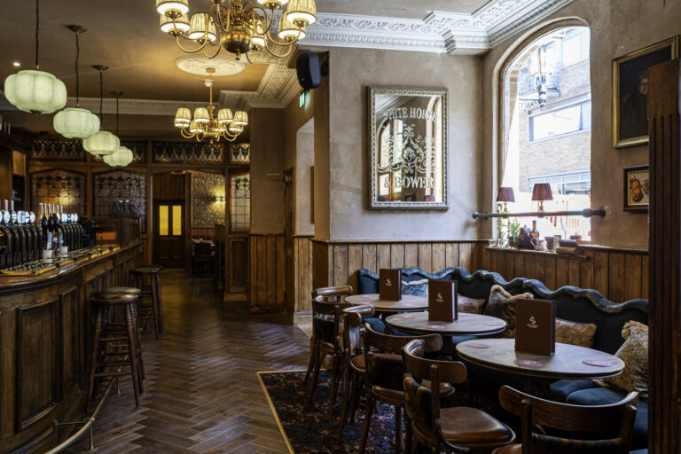 Interior of The White Horse & Bower pub in London, showing the bar, vintage chandeliers, wooden décor, and cozy seating with menus on the tables.