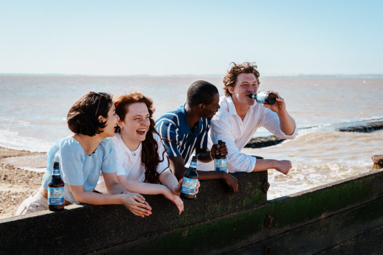 Group of friends enjoying Whitstable Bay alcohol-free beer by the seaside