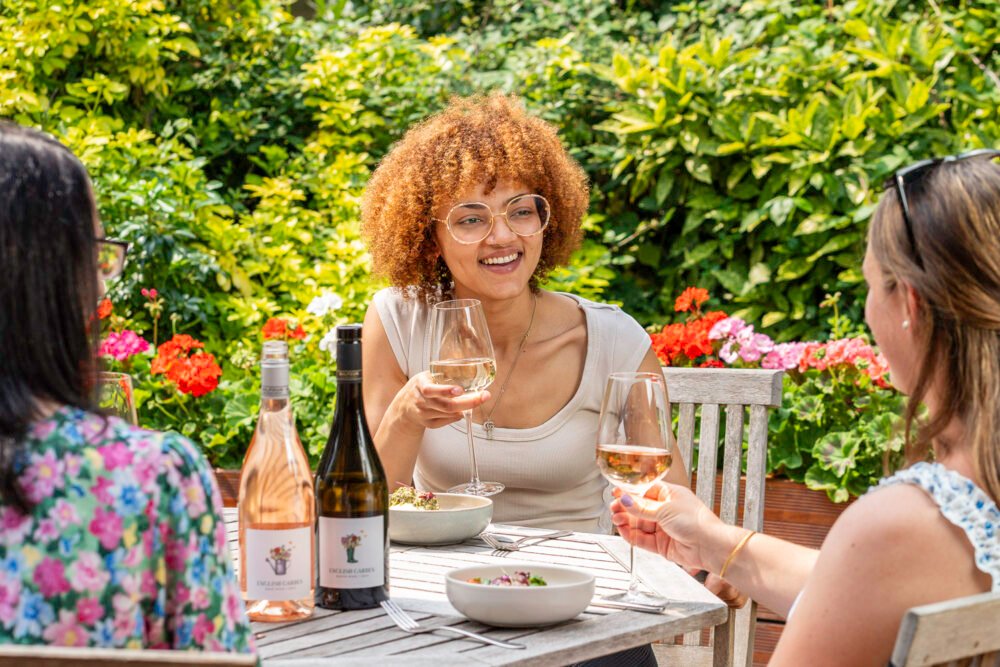 Outdoor lifestyle photo with friends enjoying wine in a summer garden. Three women enjoying wine and food in a summer garden with rosé and white wine bottles on the table