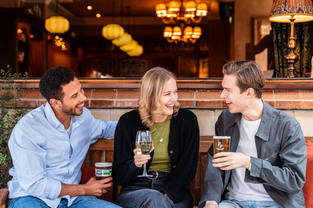 Sharing good times at The White Horse & Bower. Three friends laughing and enjoying drinks together at The White Horse & Bower pub in London.
