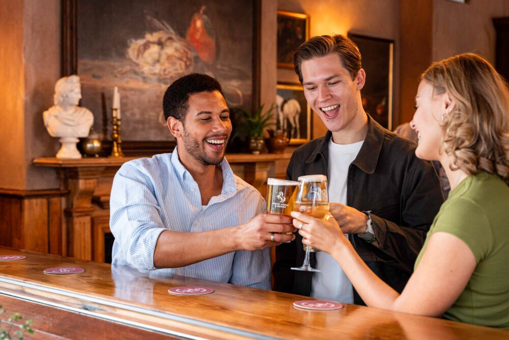 Cheers to good times at The White Horse & Bower. Three friends raising glasses and toasting with drinks at the bar inside The White Horse & Bower pub in London.