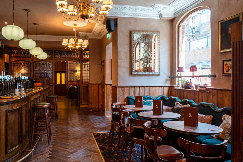 The elegant interior of The White Horse & Bower, blending tradition and comfort. Traditional pub interior at The White Horse & Bower with bar, green pendant lights and wood panelling