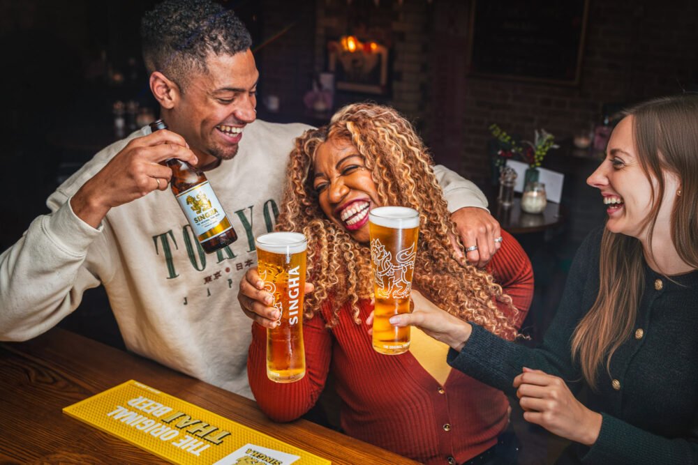Two friends laughing together over pints of First Drop beer at a pub
